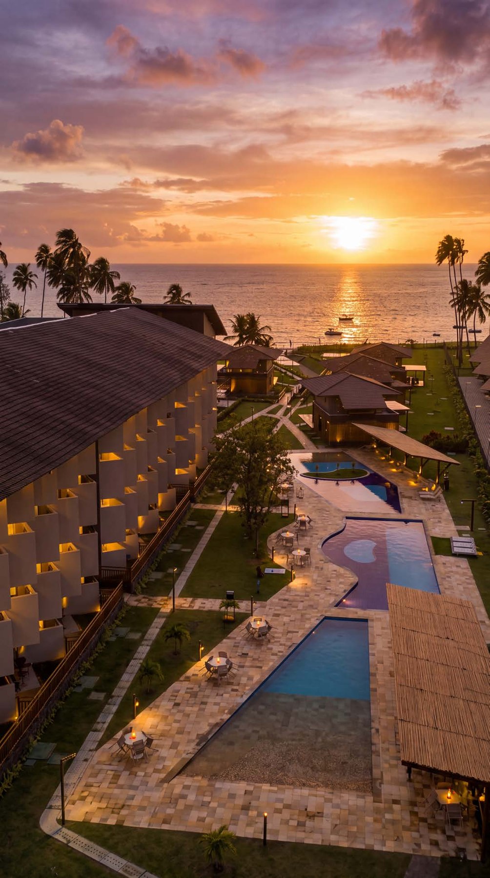 Vista do Carneiros Atlântico com piscinas, coqueiros e o mar ao pôr do sol